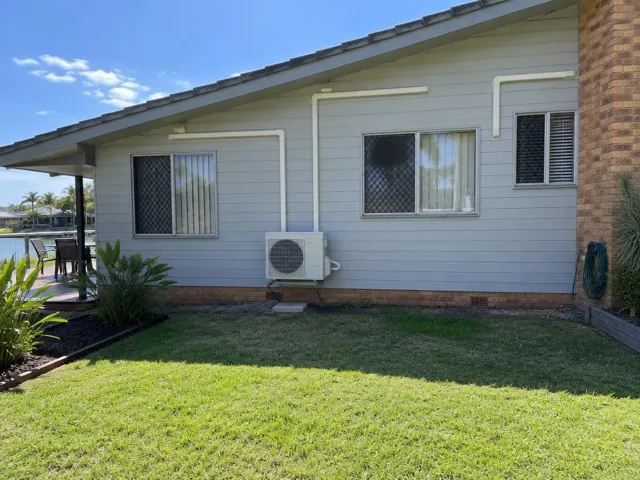 Exterior wall with one outdoor air conditioner and white pipe covers on a weatherboard home in Broadbeach Waters